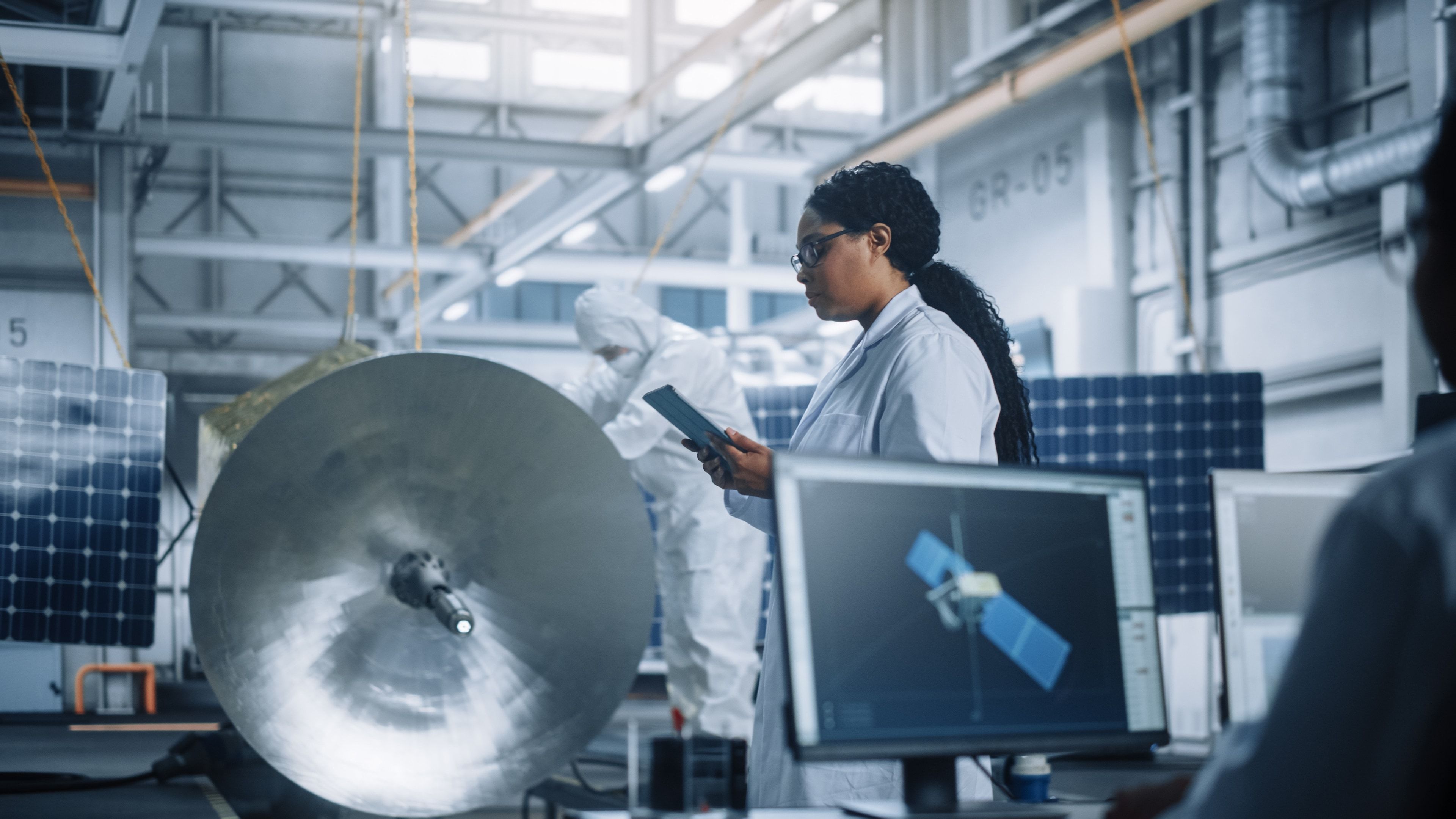 Ingeniera trabajando con una tablet en el ensamblaje de un satélite
